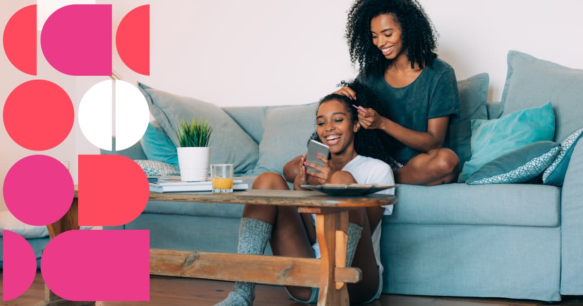 Two people relaxing on a couch together, with one styling the other’s hair while looking at a phone, beside colorful geometric shapes on the left side of the image.